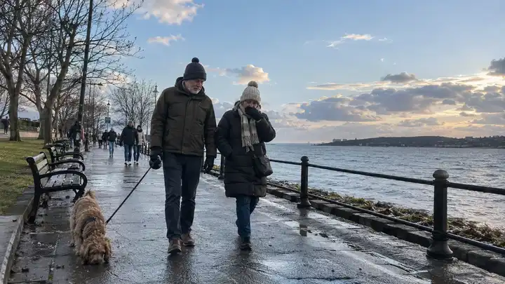Persona paseando al perro junto al mar en un día de lluvia