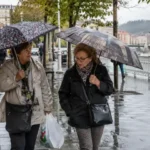 Dos mujeres mayores caminando bajo la lluvia con paraguas