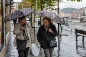 Dos mujeres mayores caminando bajo la lluvia con paraguas