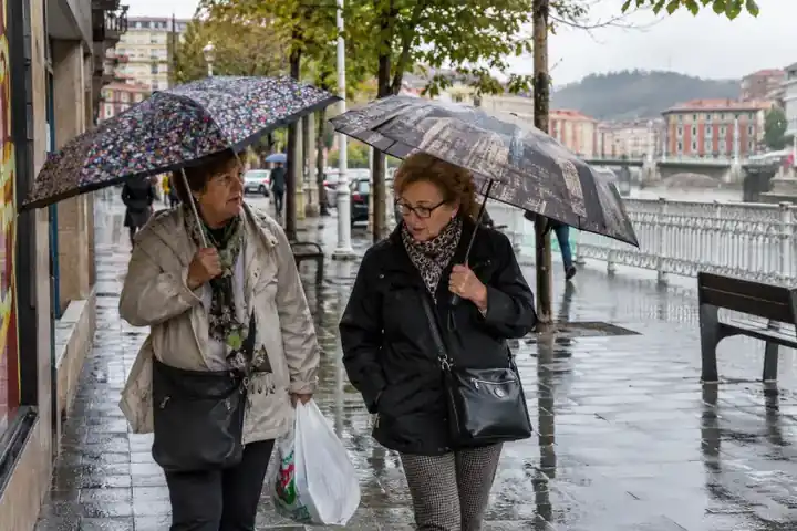 Dos mujeres mayores caminando bajo la lluvia con paraguas