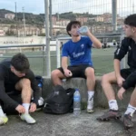 Tres jóvenes descansando junto a un campo de fútbol después de jugar