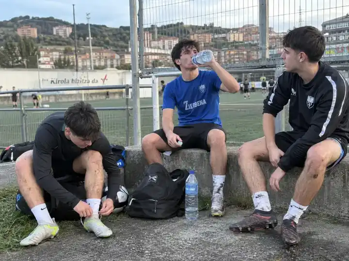 Tres jóvenes descansando junto a un campo de fútbol después de jugar