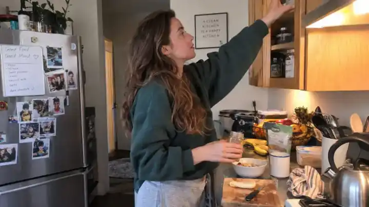 Mujer preparando comida mientras alcanza una balda alta